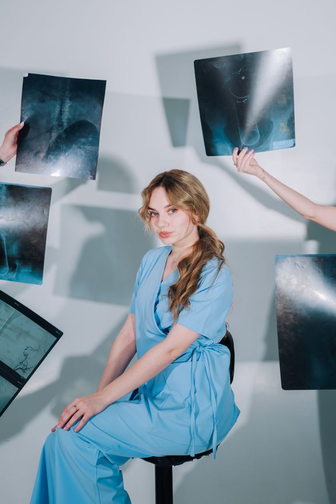 A female healthcare worker in blue scrubs reviews multiple X-ray images indoors.